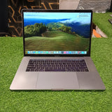 An Apple MacBook Pro with Touch Bar, displayed on a grassy surface, showing the screen turned on with a scenic wallpaper, space gray color, and a backlit keyboard.