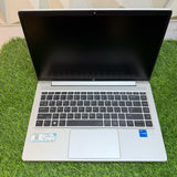 HP ProBook 440 G8 laptop with a silver color scheme, displayed on a grass-like surface against a geometric patterned backdrop.