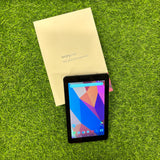 A dark grey LAVA IvoryS1 tablet computer placed on top of a flip cover, with the screen displaying colorful app icons, on a grass-like surface.