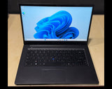 A black laptop with the screen turned on, displaying the Windows 11 desktop, placed on a light wood desk against a dark background.