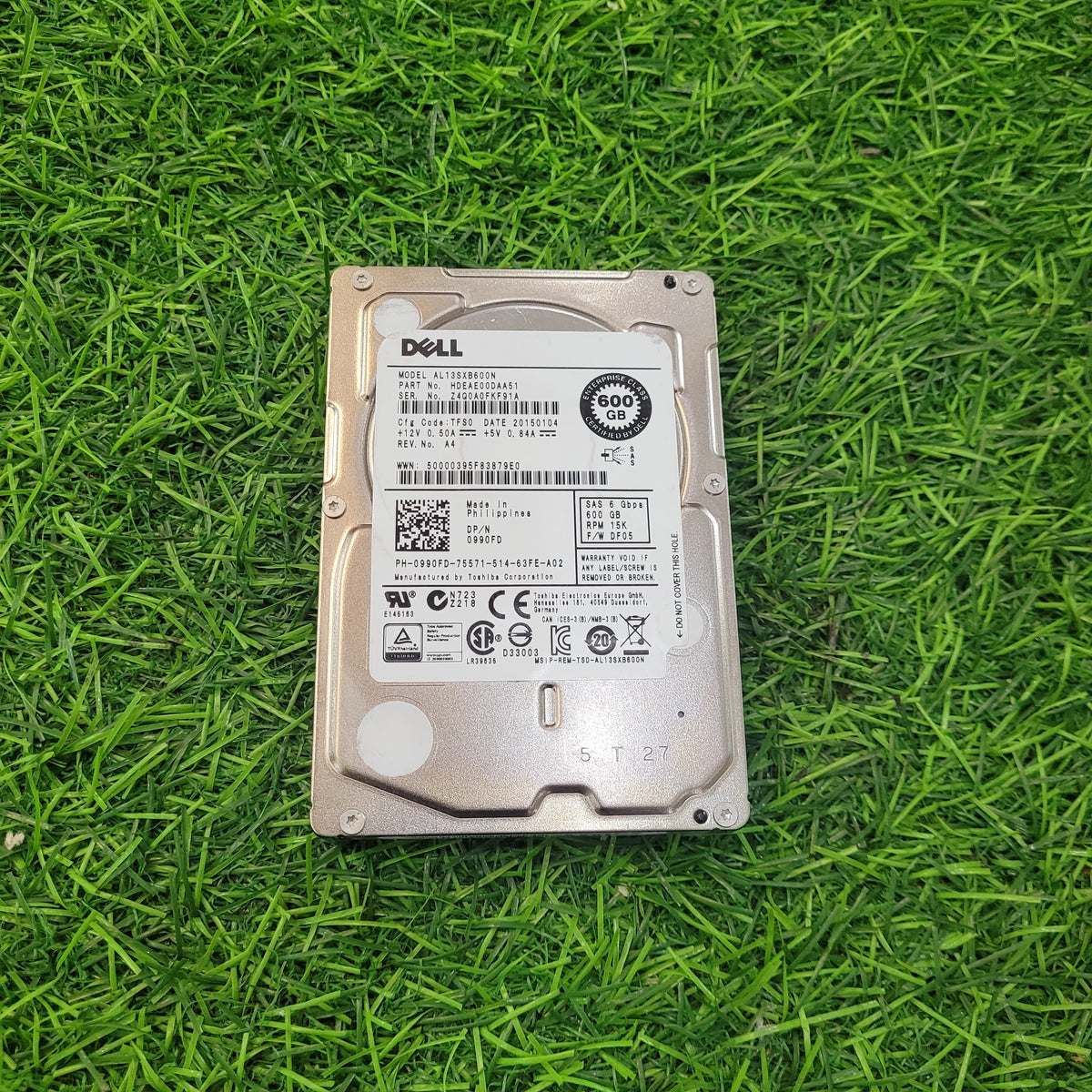 A refurbished Dell 600GB 15k RPM 6Gbps SFF serial hard disk placed on a grassy surface.
