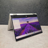 Open  HP ProBook x360 435 G8 Ryzen 7 Renewed Touchscreen Laptop displaying a scenic wallpaper on a gray surface with a dark textured wall background