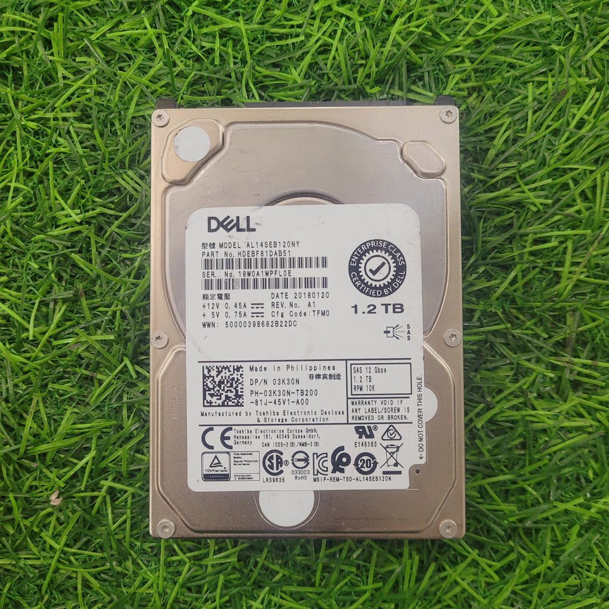 Dell 1.2TB 10K RPM 12Gbps 2.5" SAS hard drive lying on grass.