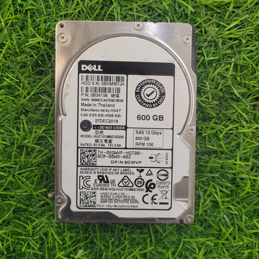 A 600GB Dell HGST hard disk drive lying on grass, showcasing its silver color and label information.