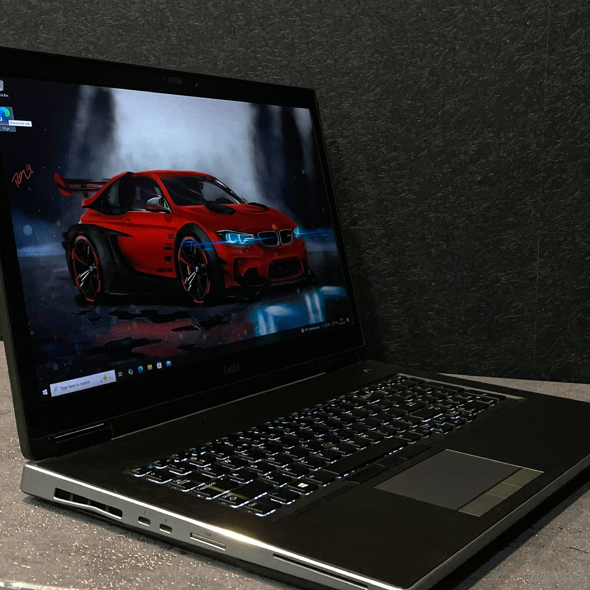 Laptop displaying a red car on a dark textured wall background