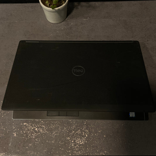 Black Dell laptop on a dark surface with a plant to the left