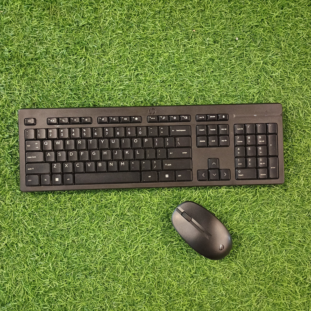 HP wireless keyboard and mouse combo on a green grass-like surface.