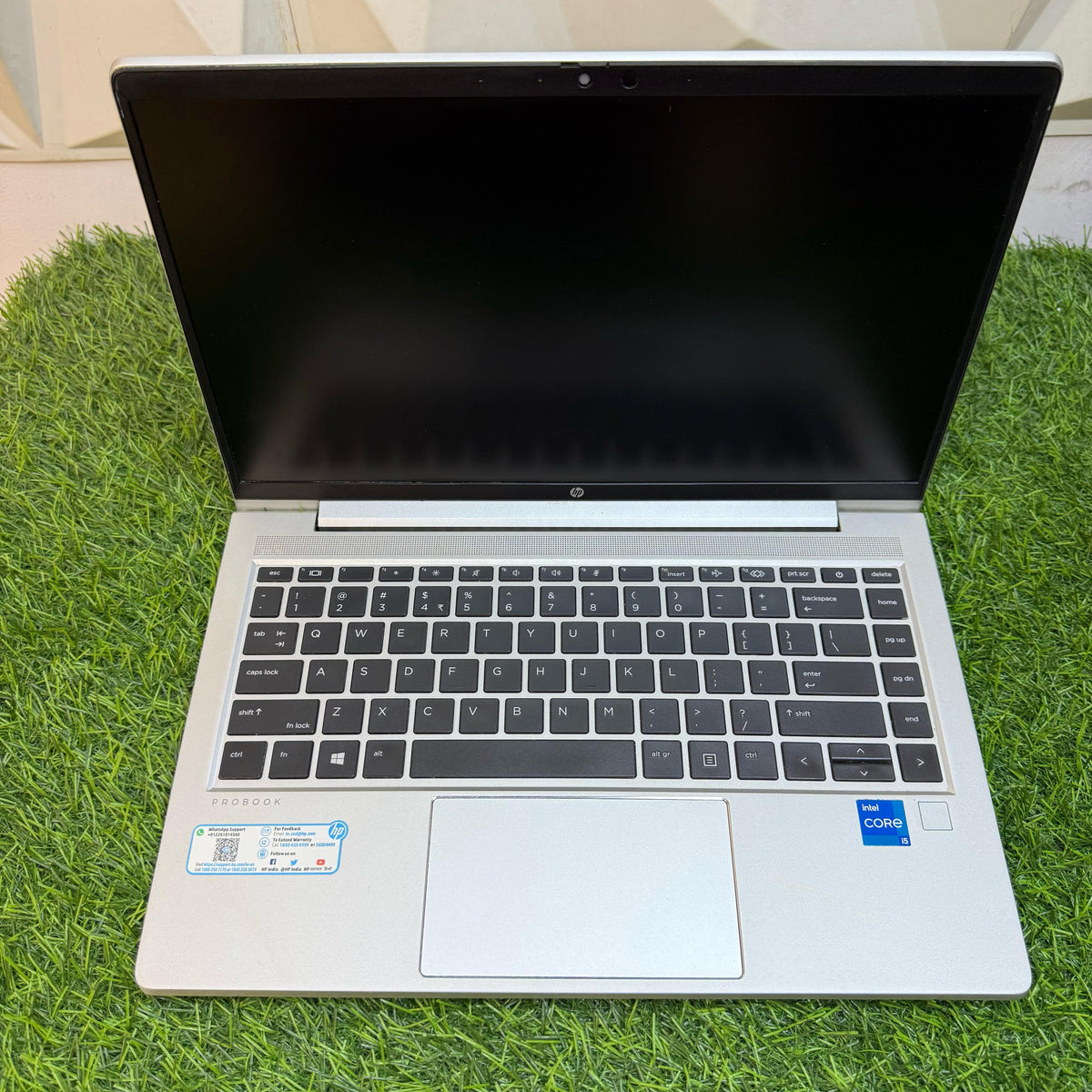 HP ProBook 440 G8 laptop with a silver color scheme, displayed on a grass-like surface against a geometric patterned backdrop.