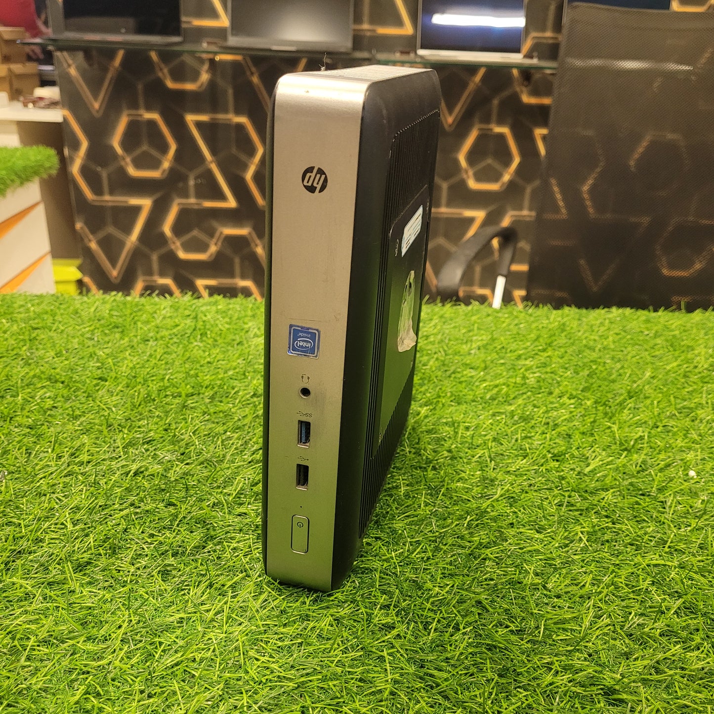HP T628 Thin Client Computer standing upright on a grass-like surface, showcasing its side profile which includes ports and branding.