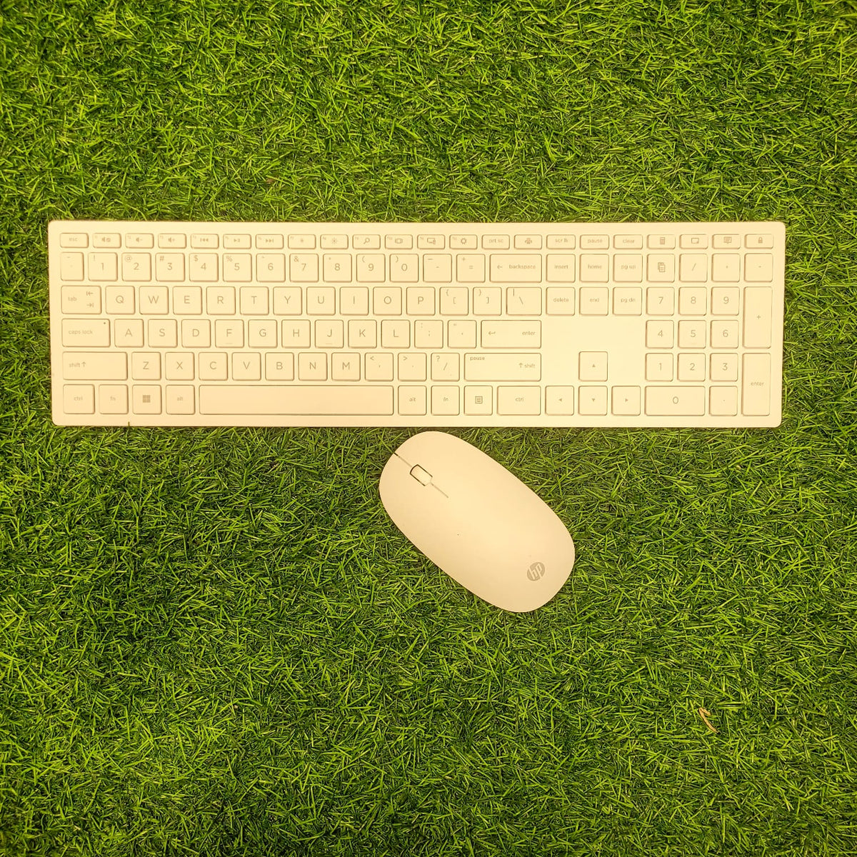 HP wireless white keyboard and mouse laid out on green grass.