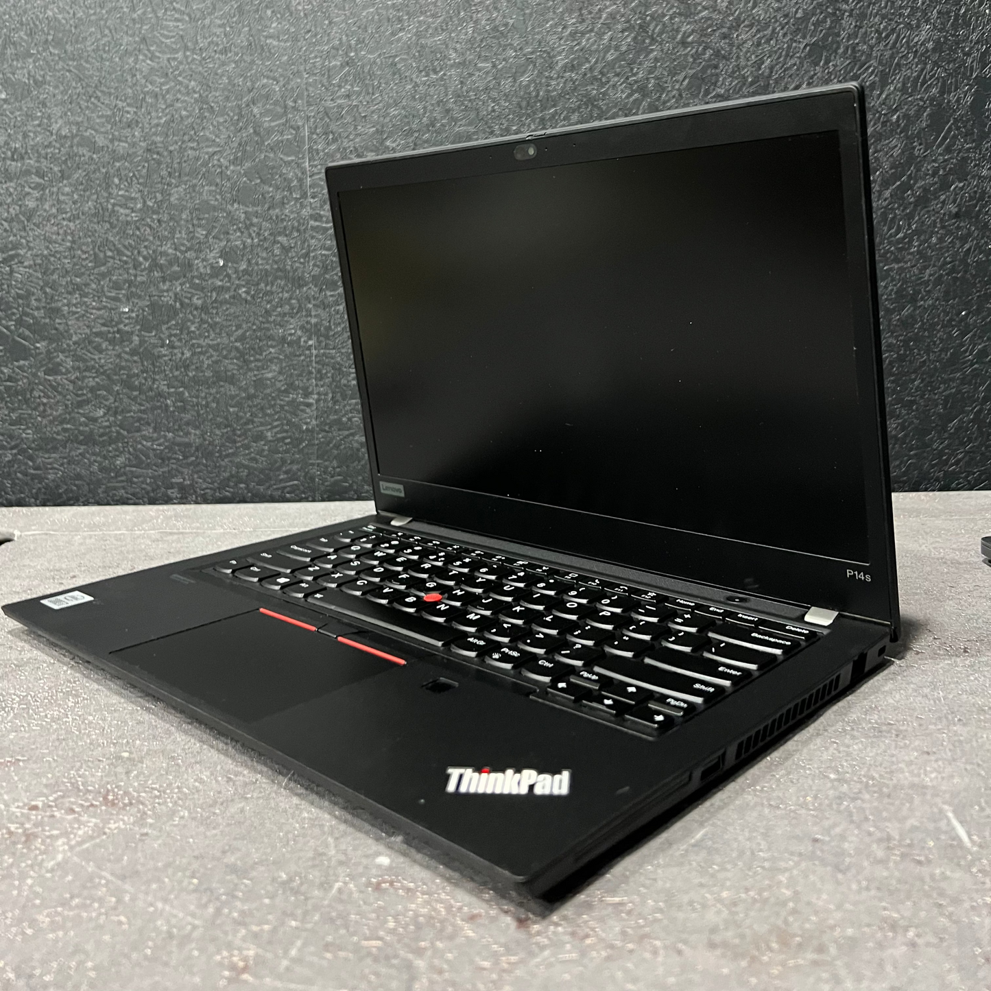Black ThinkPad laptop on a gray surface with a gray wall background