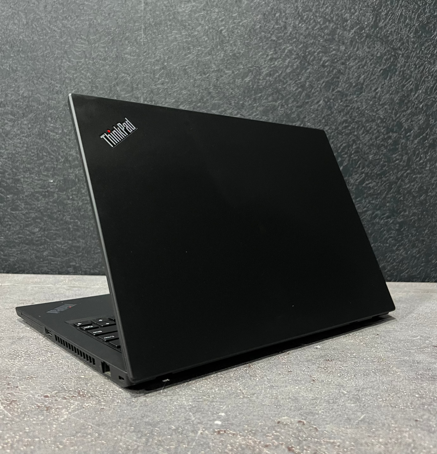 Black ThinkPad laptop on a concrete surface with a dark gray wall background