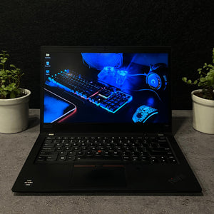 Black laptop on a dark surface with a plant on either side, displaying a blue-themed screen.