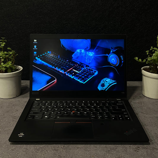 Black laptop on a dark surface with a plant on either side, displaying a blue-themed screen.