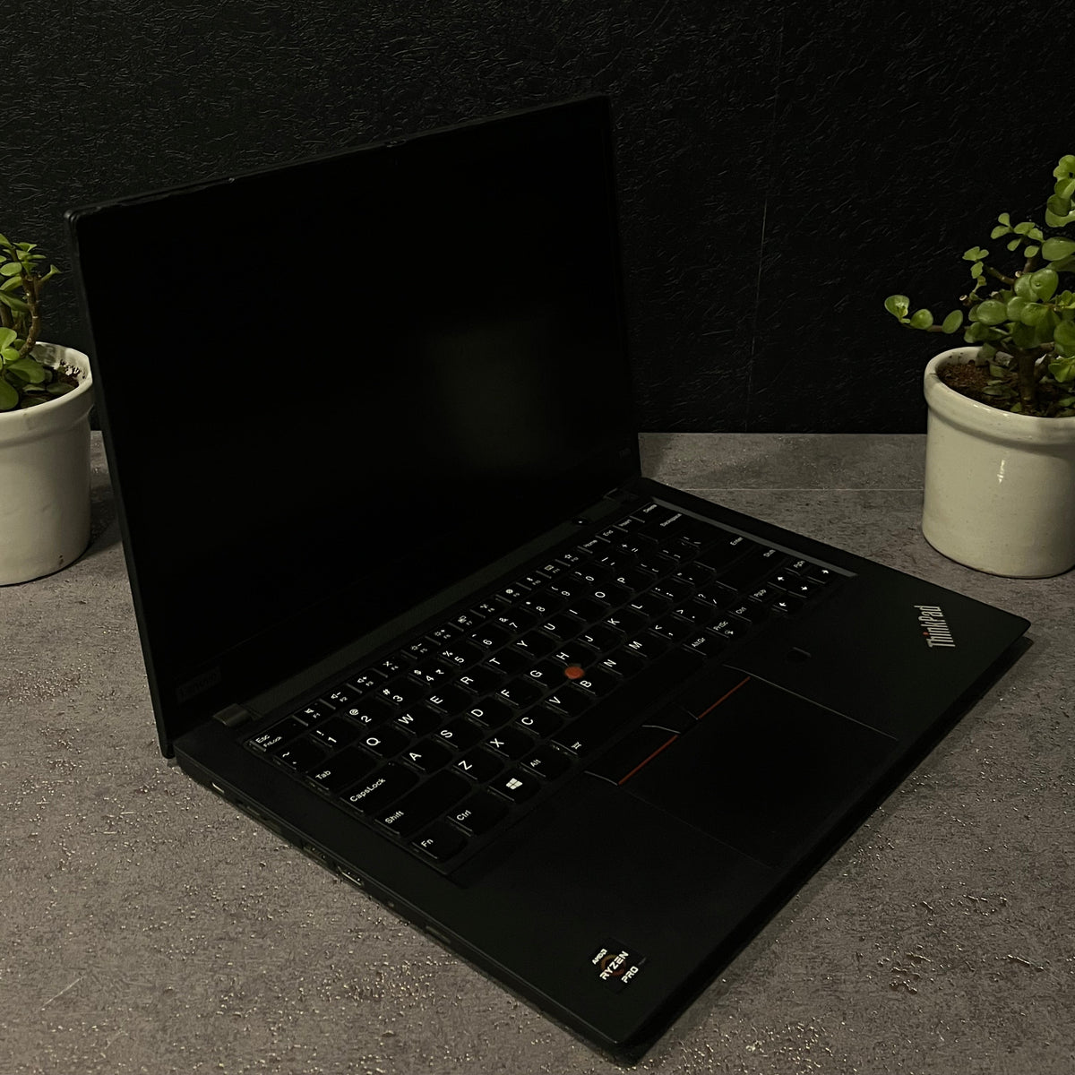 Black laptop on a dark surface with a plant in the corner