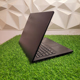A black Lenovo ThinkPad E490 laptop placed on artificial grass against a geometric patterned backdrop.