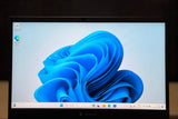 A black laptop computer displaying the Windows 11 desktop with its blue abstract wallpaper, set against a dark background.