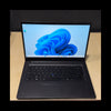 A black laptop with the screen turned on, displaying the Windows 11 desktop, placed on a light wood desk against a dark background.