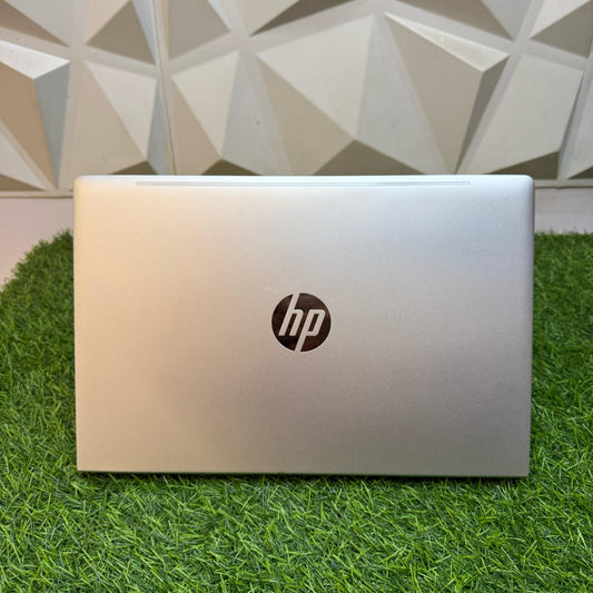 Closed silver HP ProBook 440 G8 laptop on a grass-like surface with a geometric patterned wall in the background.